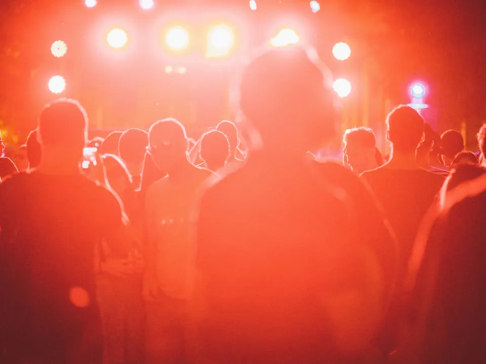 Publiek van achteren gezien voor een verlicht podium op een avondfestival